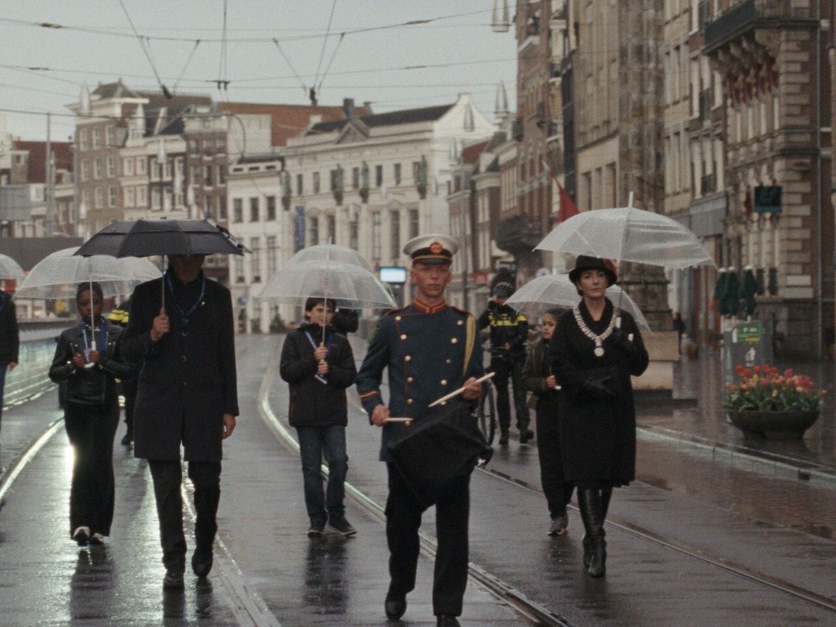 an archival image of a group of people holding umbrellas behind a drummer walking down an empty street.