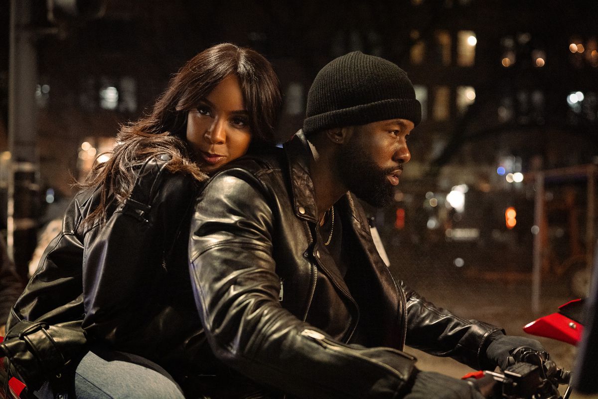 A woman riding on the back of a motorcycle with a bearded man in a leather coat and beanie hat driving.