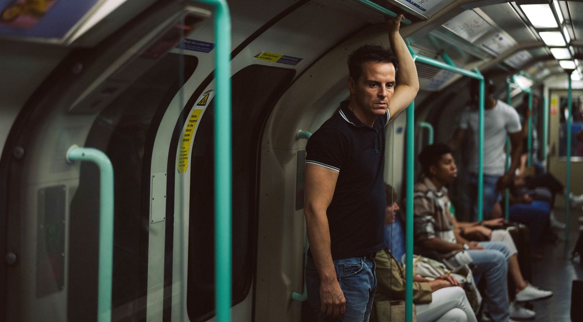 Adam (Andrew Scott) stands alone on a subway car, hanging onto the overhead railing, looking drained and haggard in All of Us Strangers