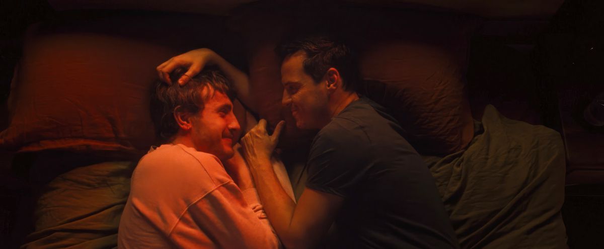 Harry (Paul Mescal) and Adam (Andrew Scott) curl up together, face to face in a red-lit bed, in All of Us Strangers