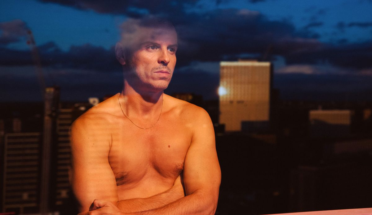 Adam (Andrew Scott) stands shirtless and pensive in front of a window in his high-rise apartment in All of Us Strangers