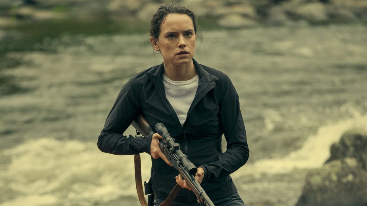Daisy Ridley holding a rifle while standing in front of a river in The Marsh King’s Daughter.