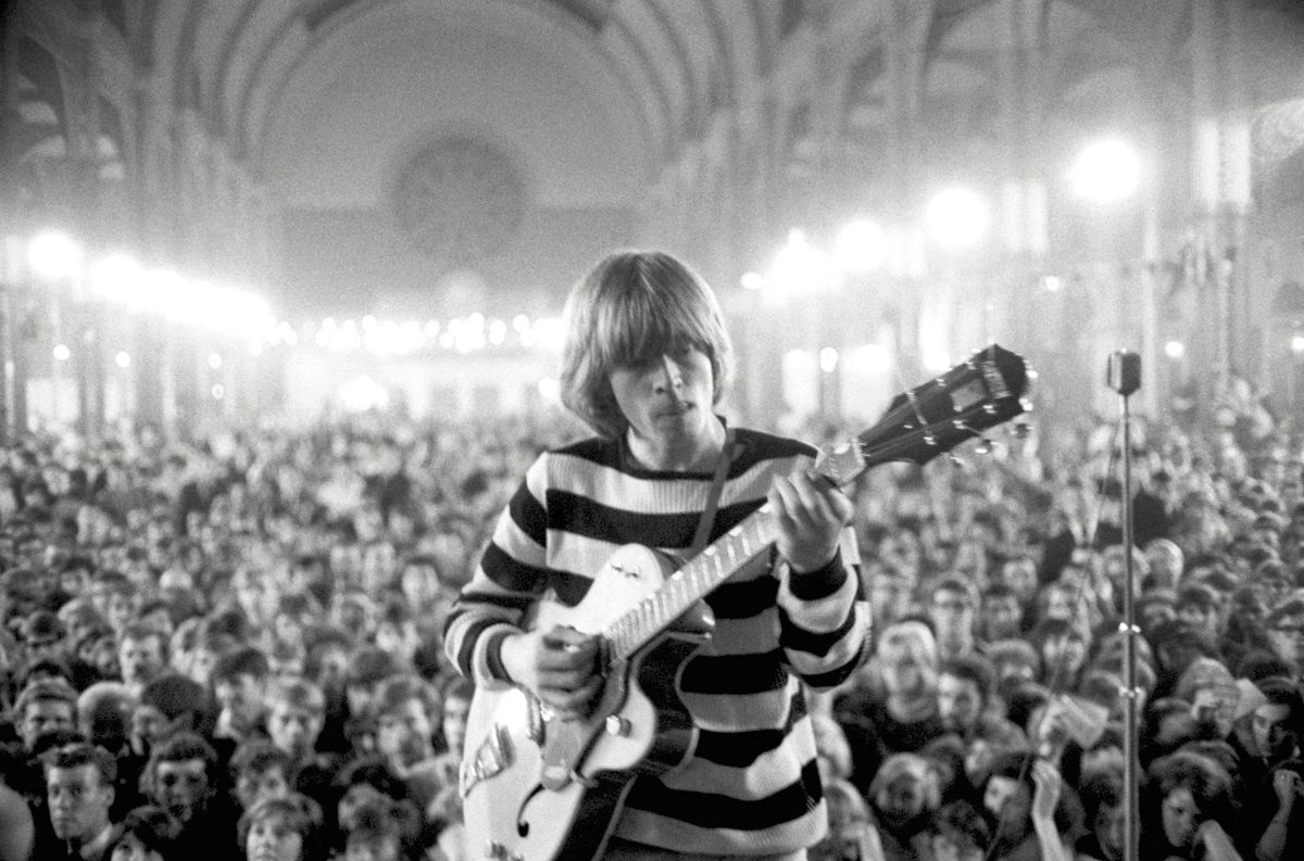 Photo of Brian Jones in front of a packed theater playing the guitar in The Stones &amp; Brian Jones.