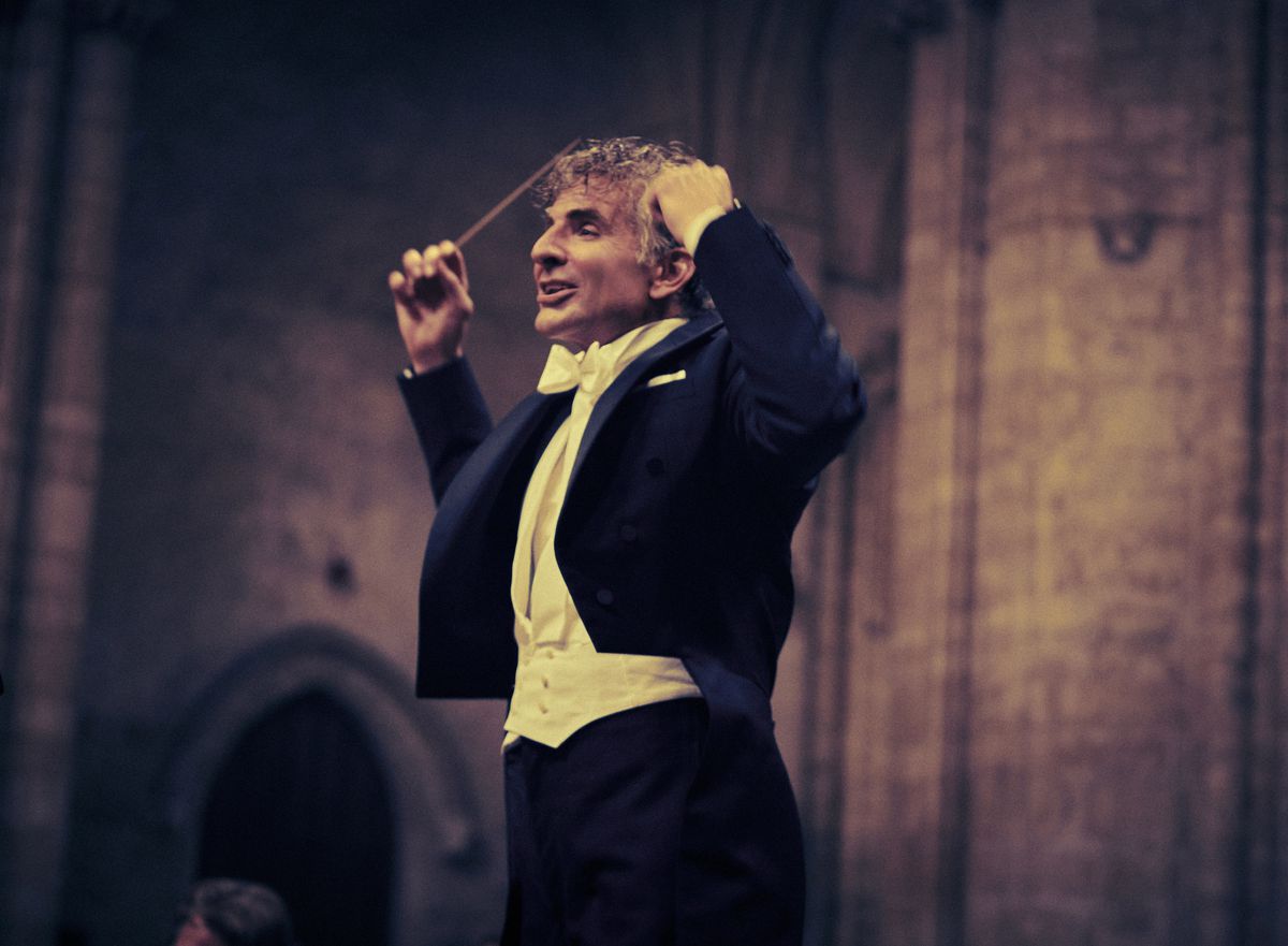 Bradley Cooper as Leonard Bernstein conducting in a tuxedo in Maestro