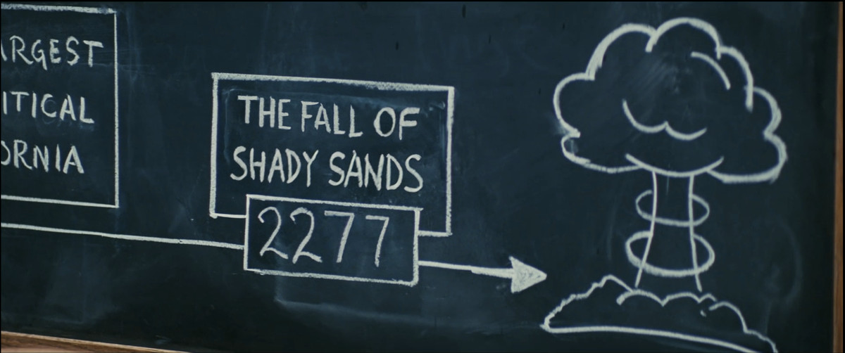 Fallout 시즌 1의 스크린샷, 원자 폭탄 폭발 그림을 가리키는 화살표와 함께 "The Fall of Shady Sands: 2277"이라고 적힌 칠판 그림
