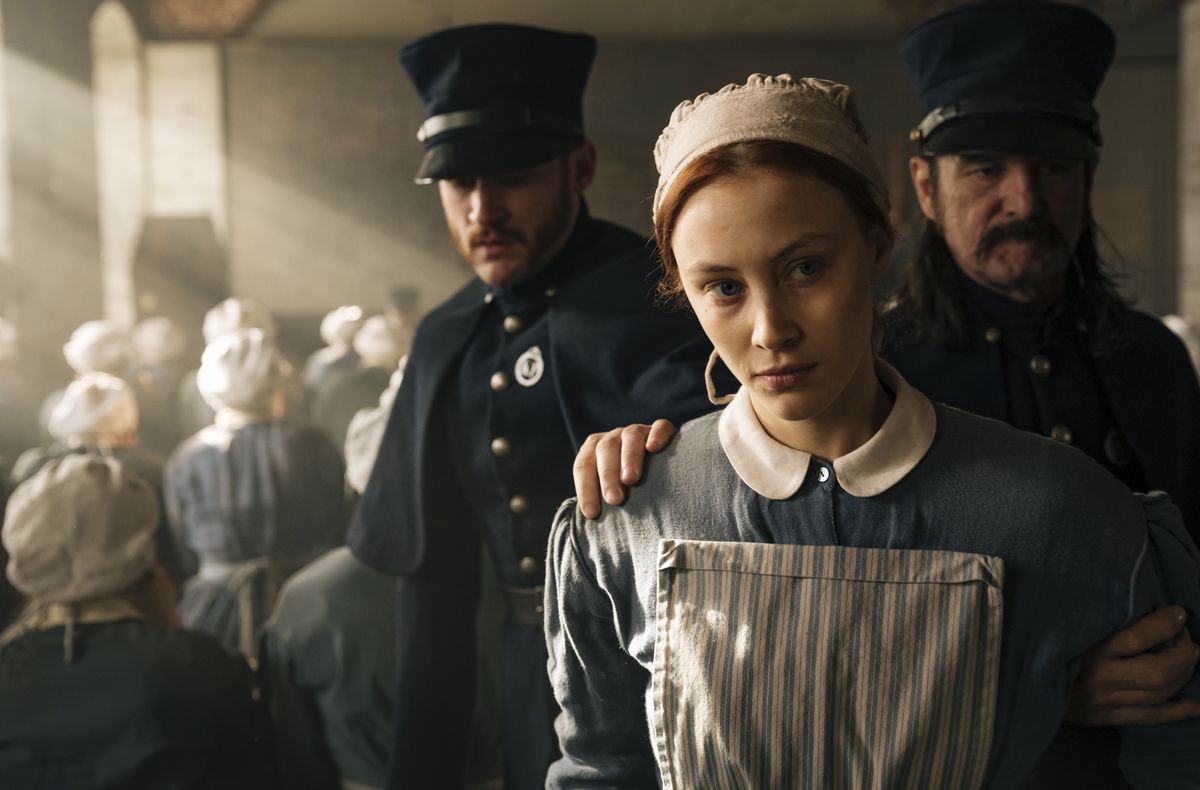Sarah Gadon, wearing mid 19th-century colonial garb, is led away by police officers in Alias Grace.
